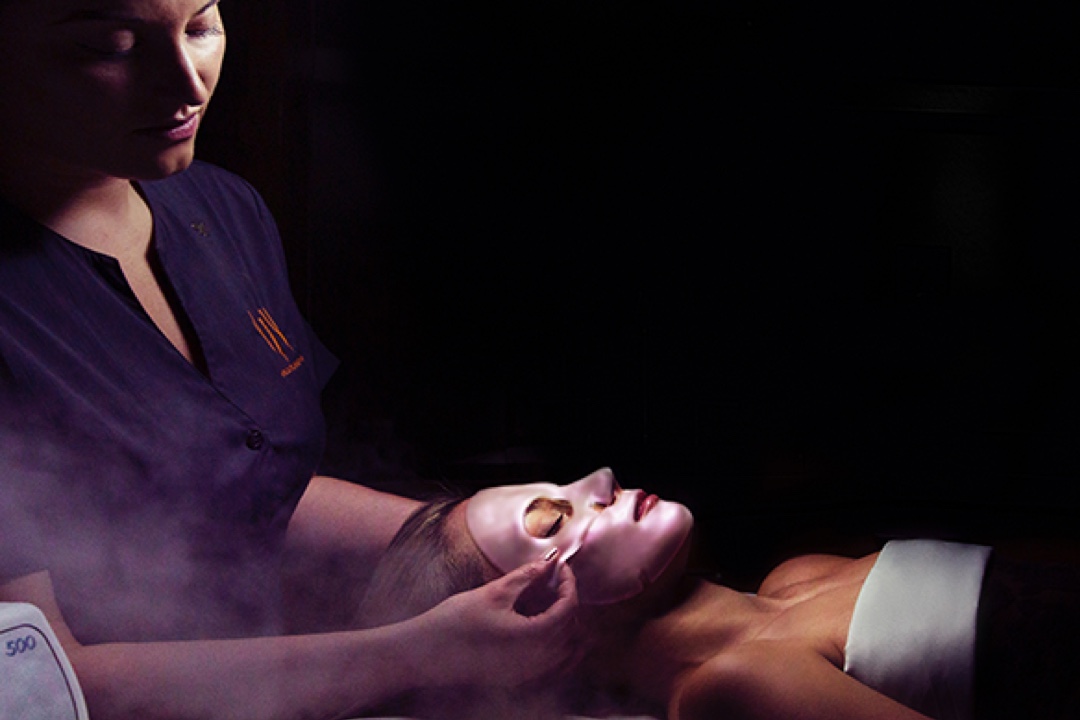 a woman getting a spa treatment. she is laying down and having a face mask being applied by a specialist.
