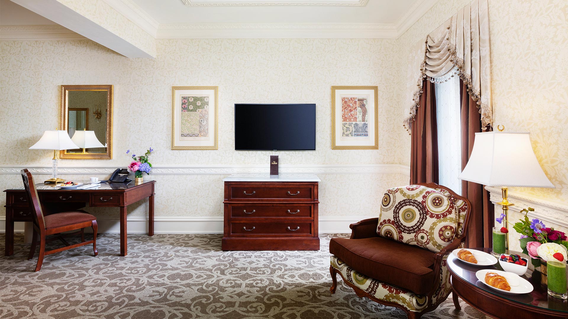 sitting area with a desk, tv, dresser and chairs. there is breakfast on the side table between the two chairs