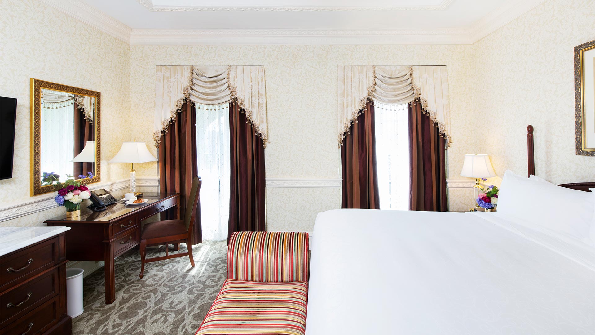 interior shot of the bedroom area. There is a king bed with a desk, TV and sitting bench at the foot of the bed. Two windows give views of the resort.