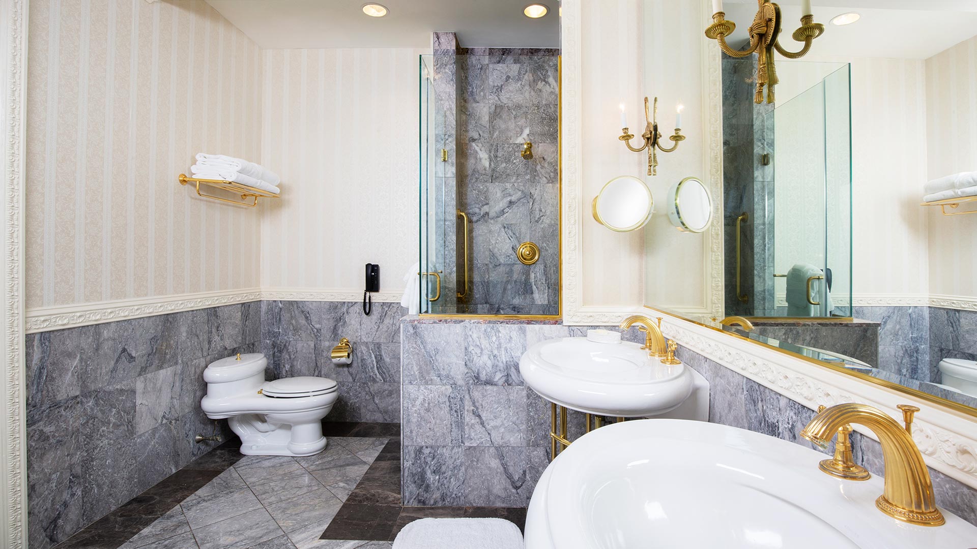 interior of the suite's bathroom. the room has neutral gray tiling, two sinks, a large mirror, and a walk in shower.