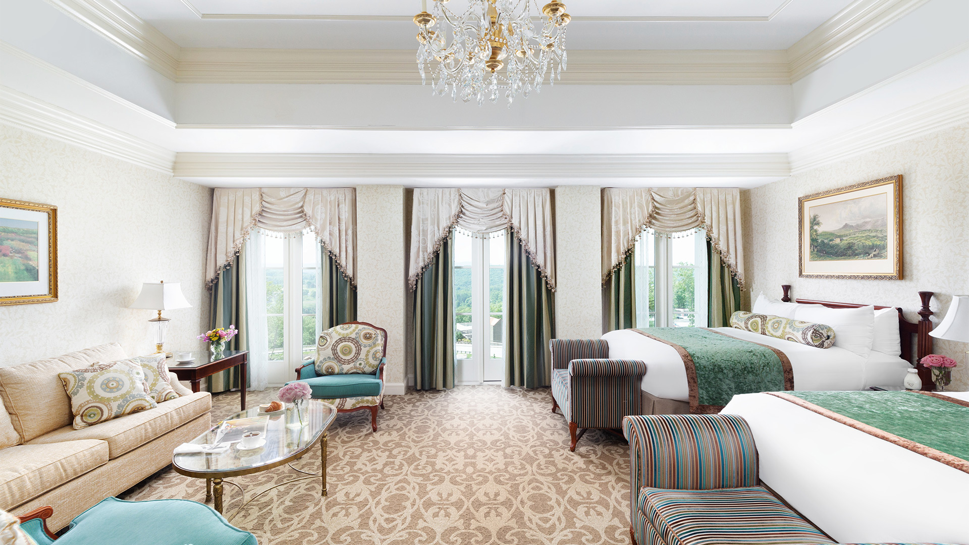 interior shot of The Chateau's junior double room. There are two queen beds with green and white linens and sitting benches at the foot of each. There are three windows overlooking the resort grounds and a sitting area