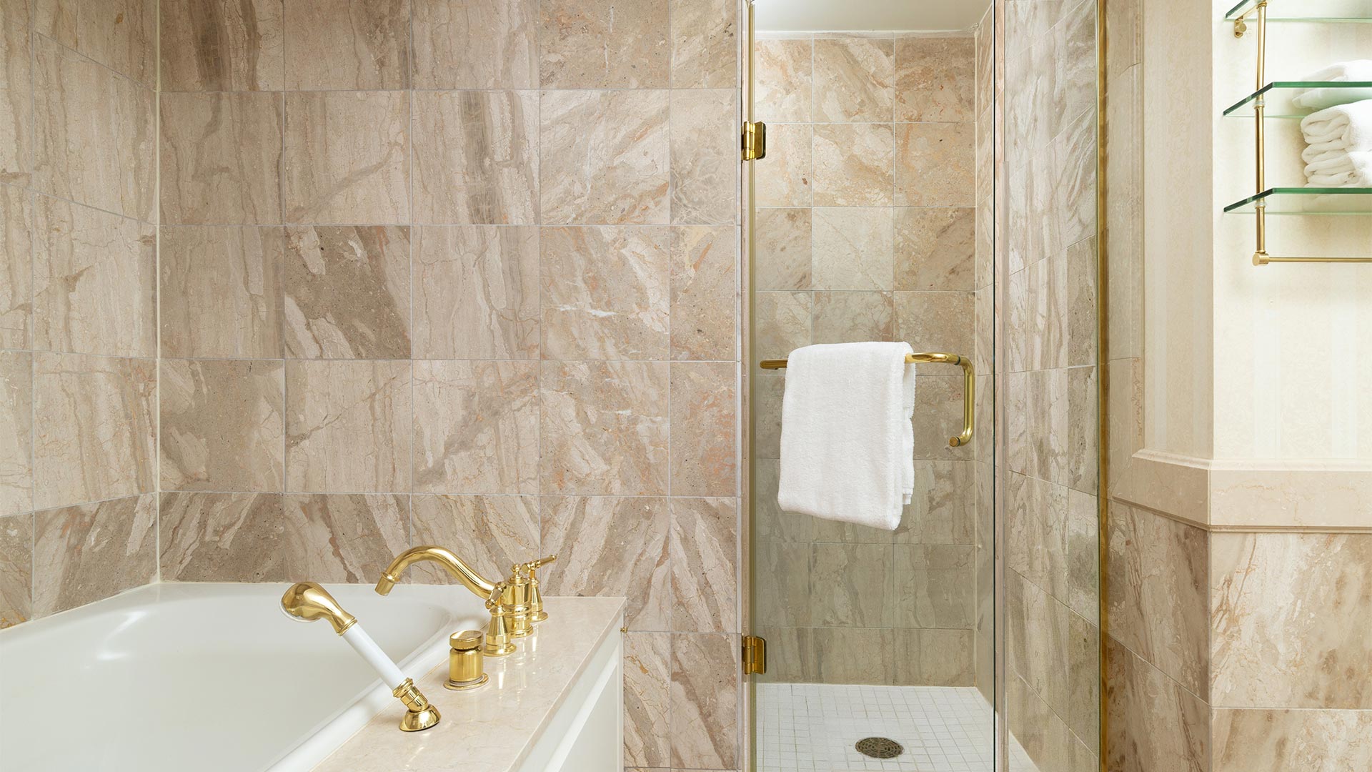 detail shot of the bathroom. The tiling is a neutral beige and the whirlpool bathtub is white with gold hardware. There is also a small shower next to the bathtub.