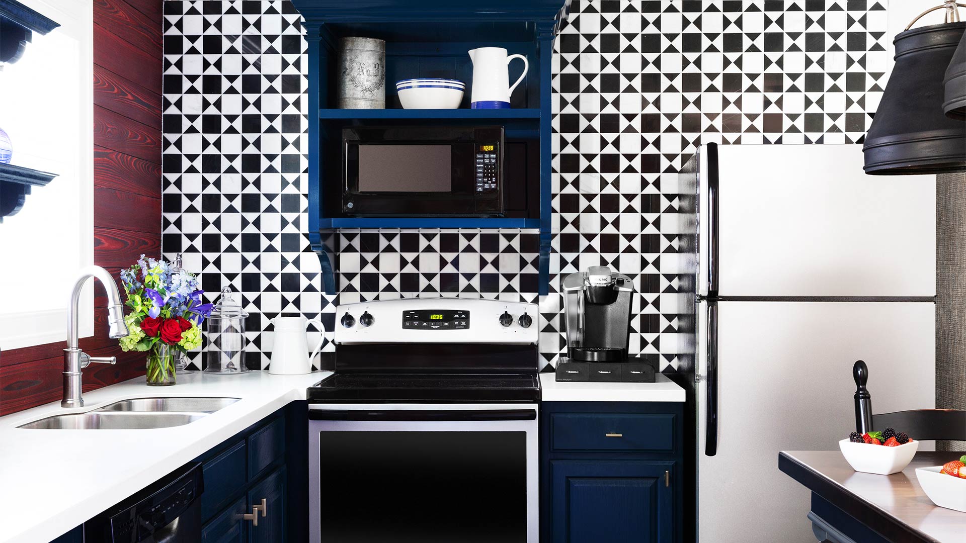 an interior shot of the full kitchen in the townhomes. The tiling is a geometric black and white print. There is a sink, a full fridge, an over and stovetop. There is ample counter and storage space.