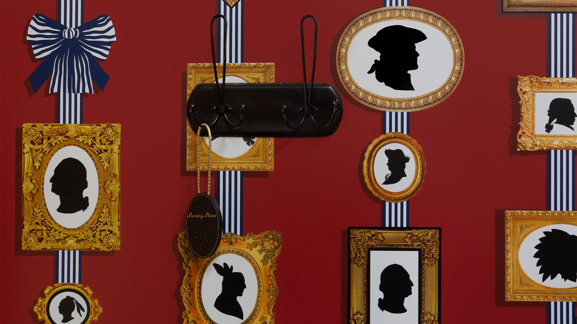 detail shot of a wall. The wall is a deep red color with gold framed pictures of silhouettes of colonial-era people