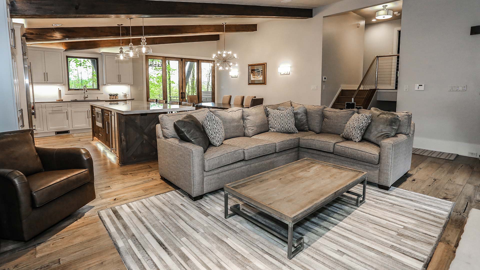 interior shot of greystone's living area. The colors in the room are a neutral gray tone. There is a plush couch surrounding a wooden coffee table. It is an open floor plan with exposed wooden beams on the ceiling.