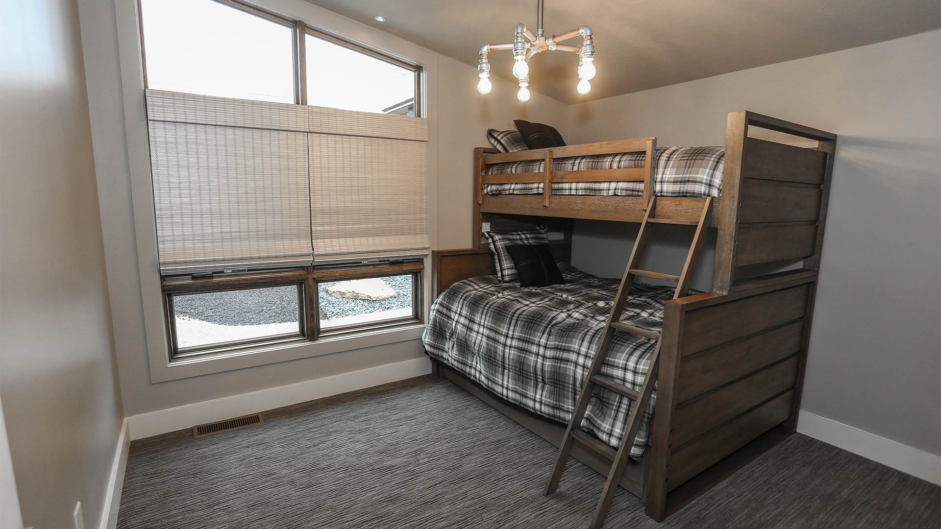 interior shot of a bedroom with bunkbeds. The bunkbeds have grey plaid bedding. There are large windows giving views of the nature outside