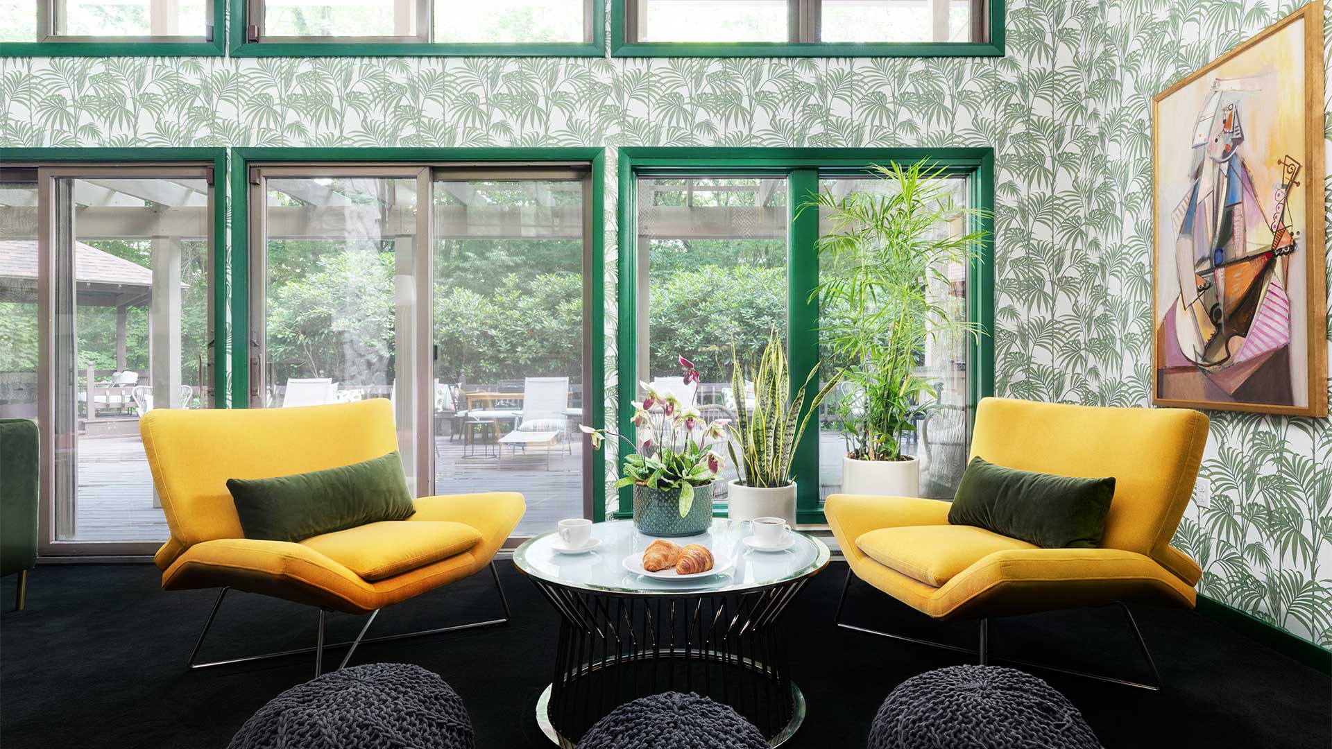 a sitting area with two canary yellow retro-inspired chairs. There is a circular table in between the two chairs with potted plants resting on top. There is a sliding glass door leading out to a patio.