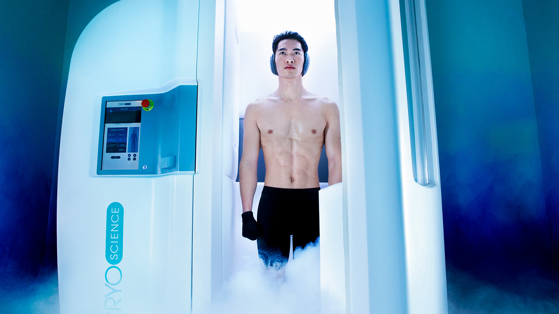 a shirtless man is walking out of a white chamber. The lighting is blue and there is steam coming out of the chamber