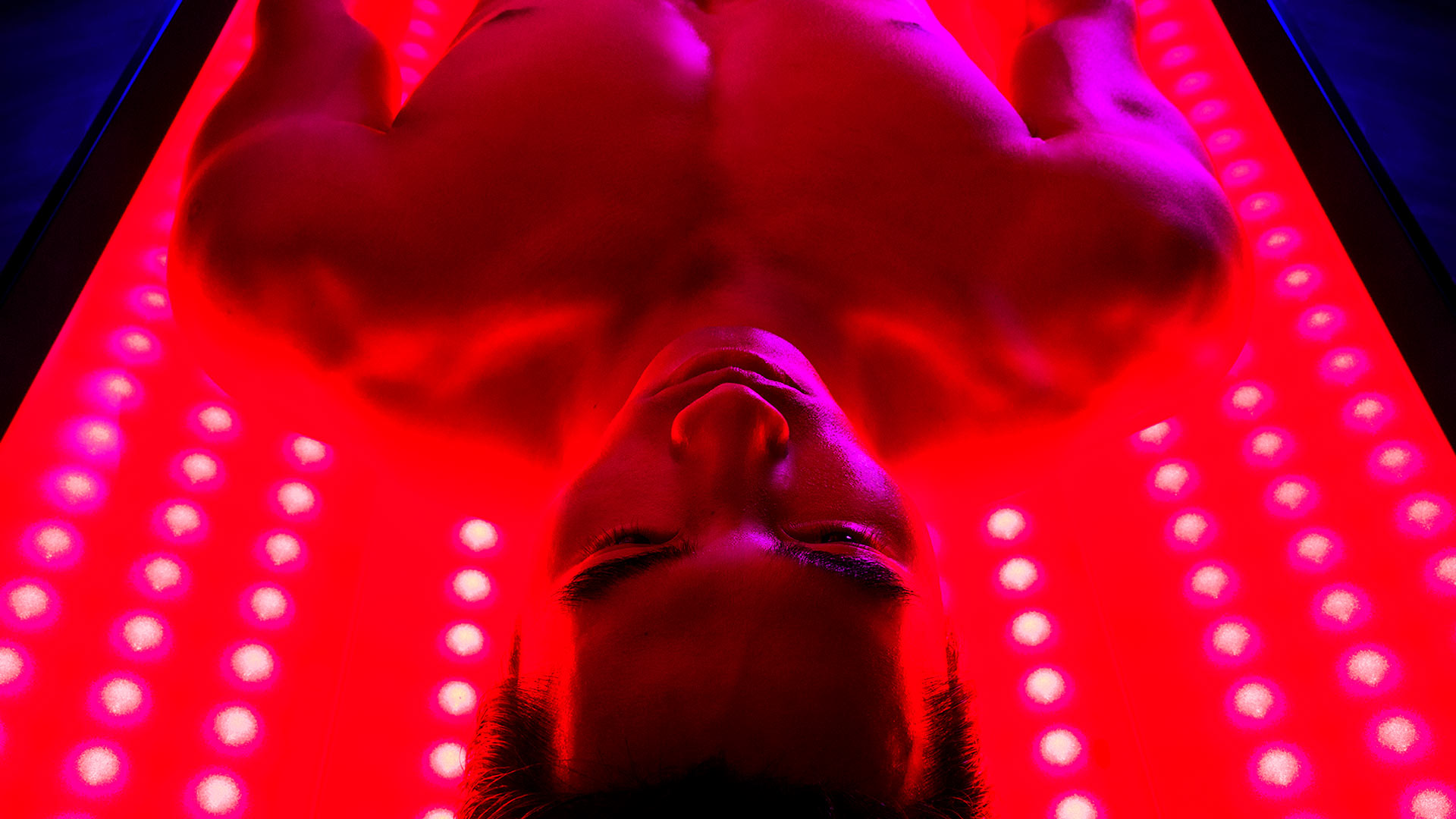 a close up shot of a man lying on his back in a chamber. There is infrared light shining on him