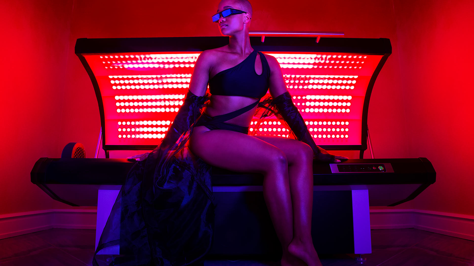 a woman dressed in a fashionable black bikini is sitting on a infrared light bed