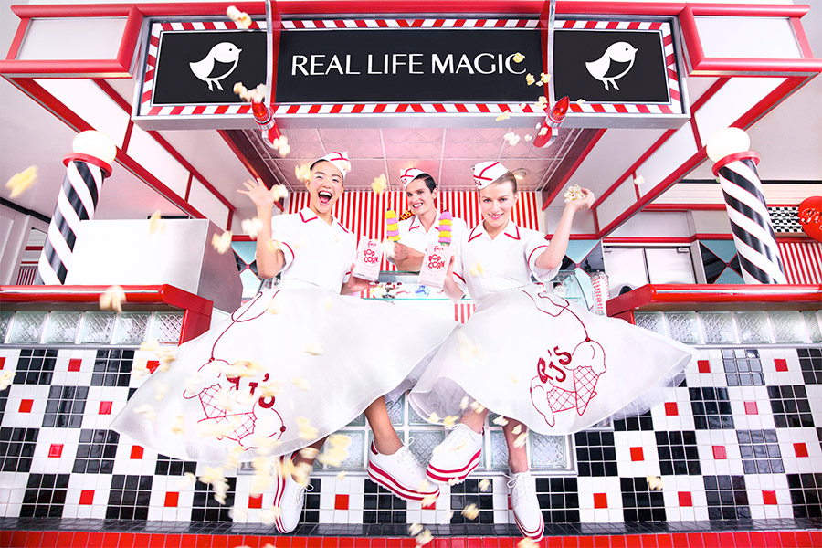 "Real Life Magic" sign above three girls in big skirts and hats serving ice cream