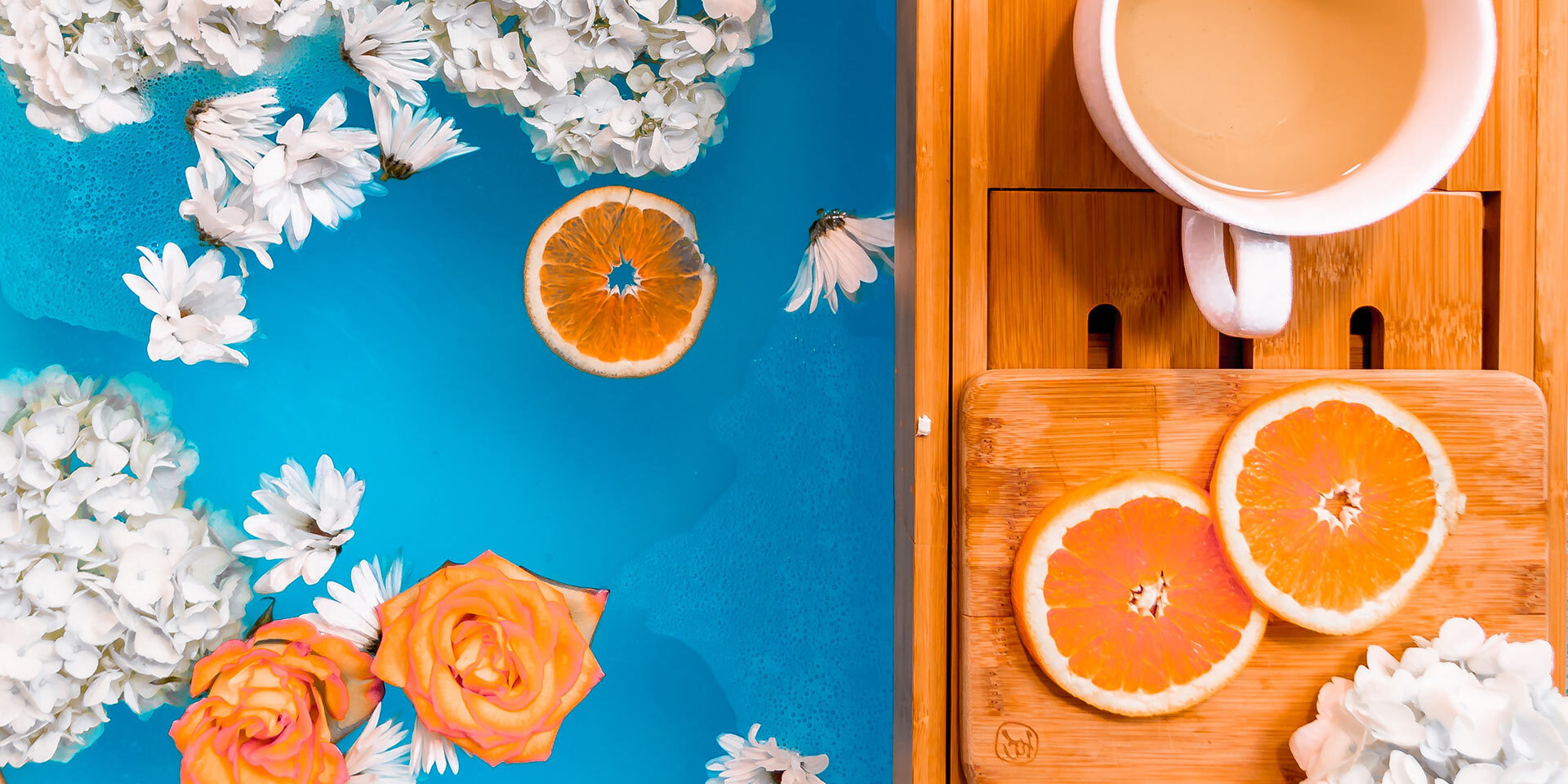 orange slices and flowers in water next to wood with tea cup on it