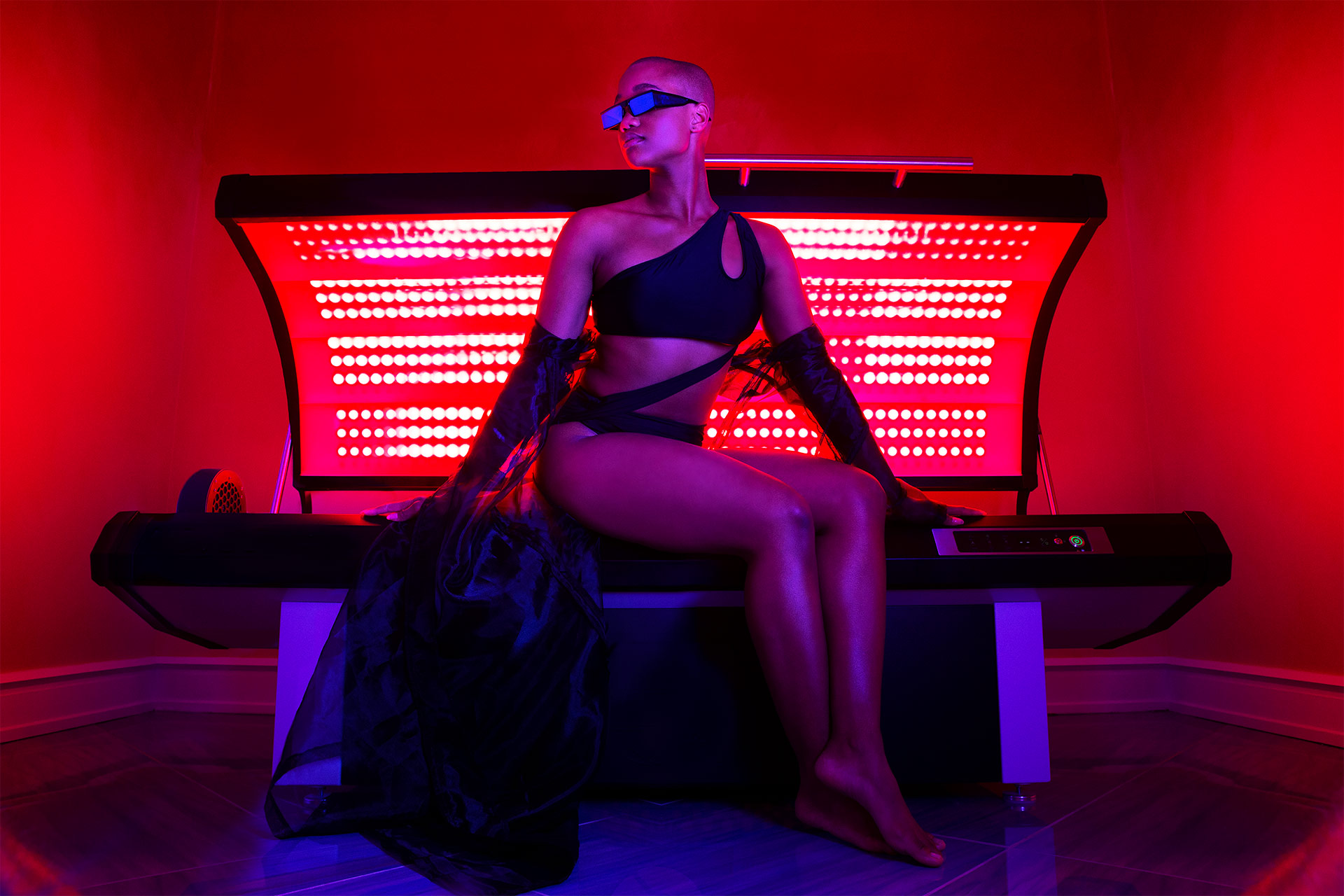 A woman in a red room sitting on top of a tanning bed with red lights within