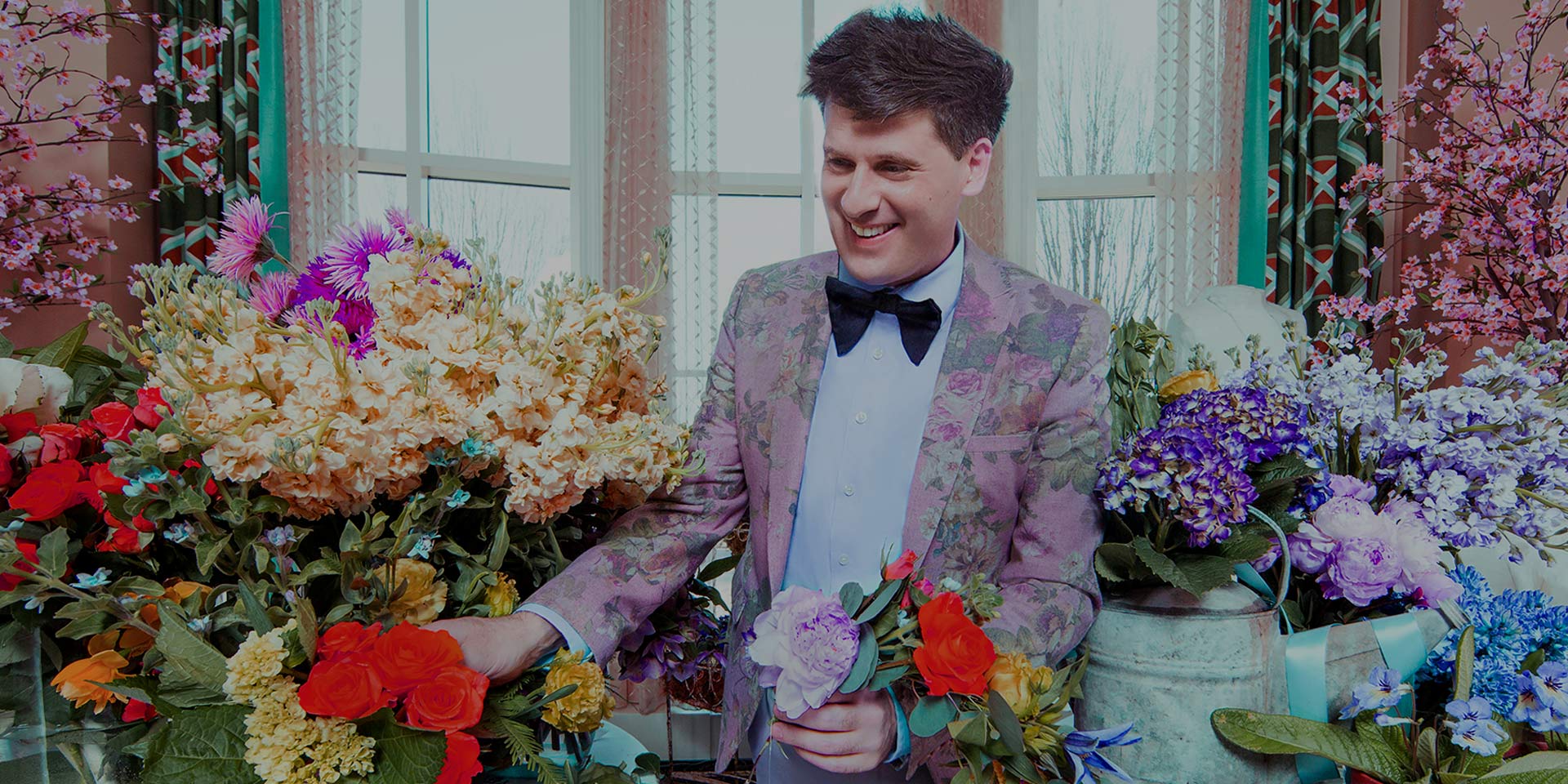 man in pastel suit and bowtie surrounded by flowers