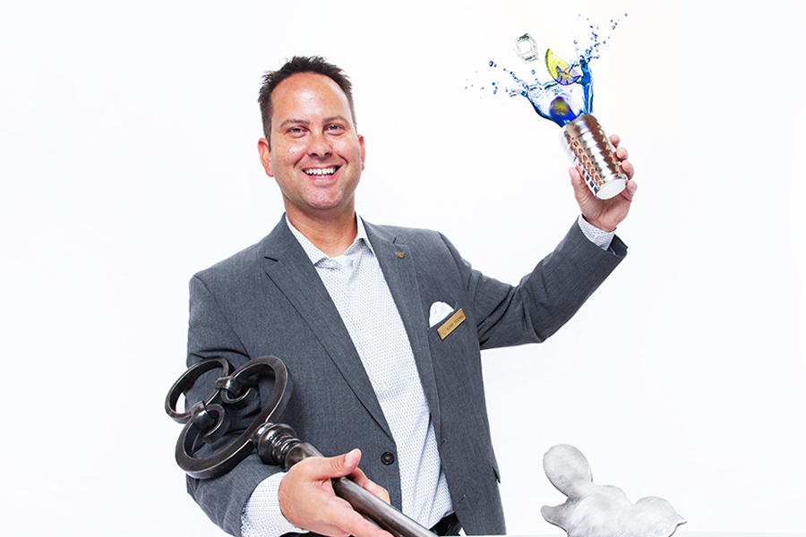 Smiling man throwing up a cup of blue liquid with lime in it and holding a giant key