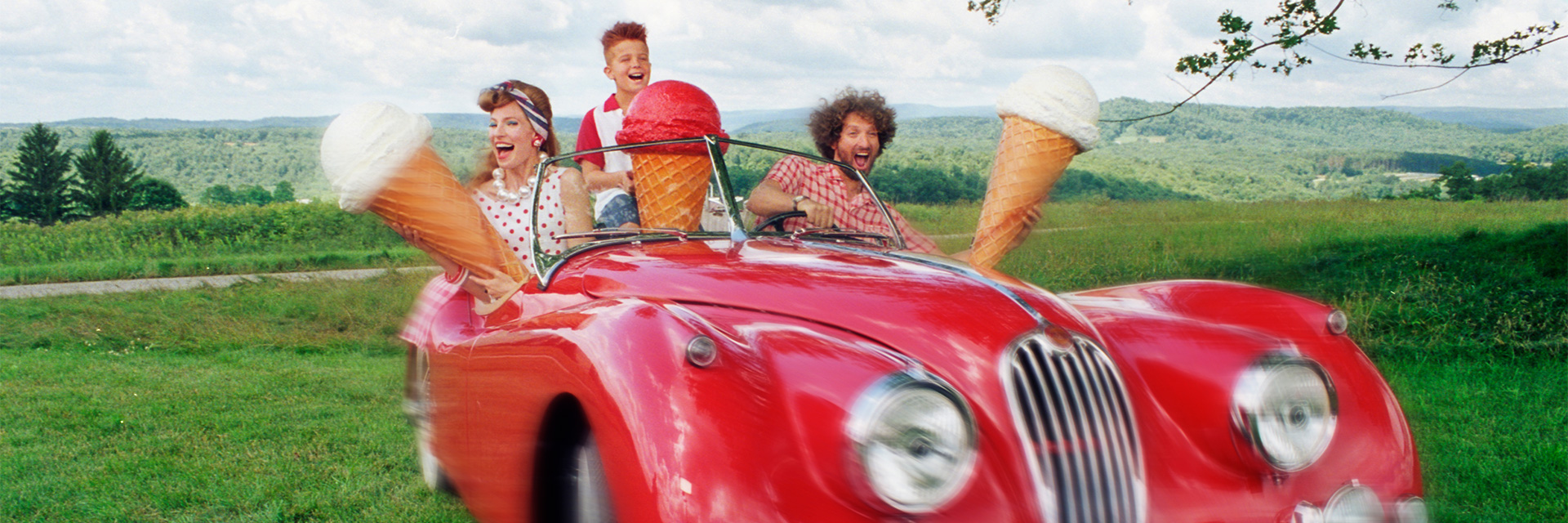 a family in a vintage red car in a field holding up giant ice cream cones
