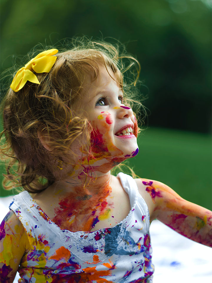 A little girl with paint all over herself smiling.